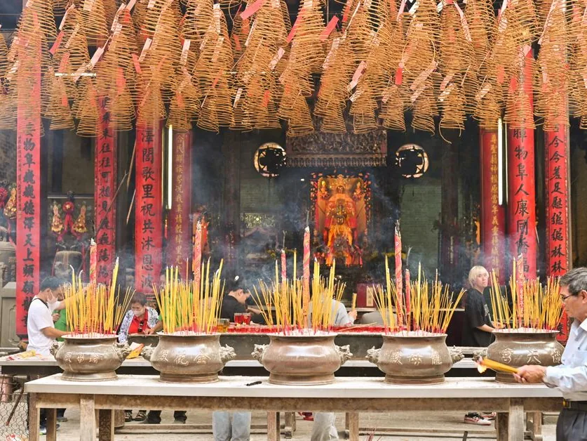 A Chinese temple interior with hanging spiral incense coils and worshippers